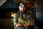 Portrait of a brutal, confident blacksmith, a man with a beard. Standing in the workshop, folding his arms over his chest